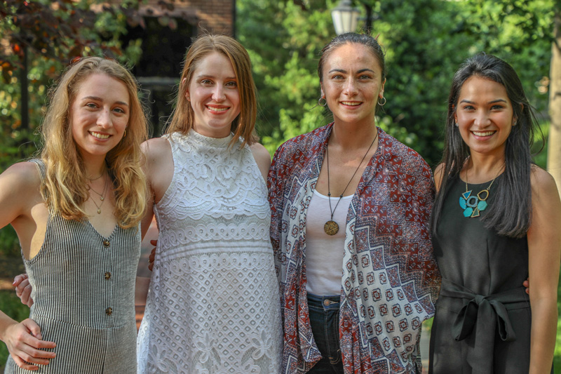Four women standing side-by-side, with their arms around each other.