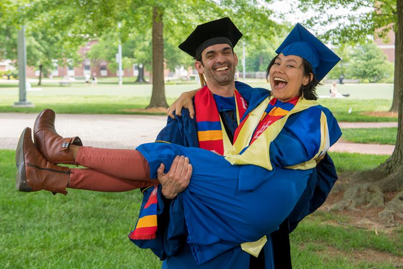 a student wearing a cap and gown holds another student in a cap and gown