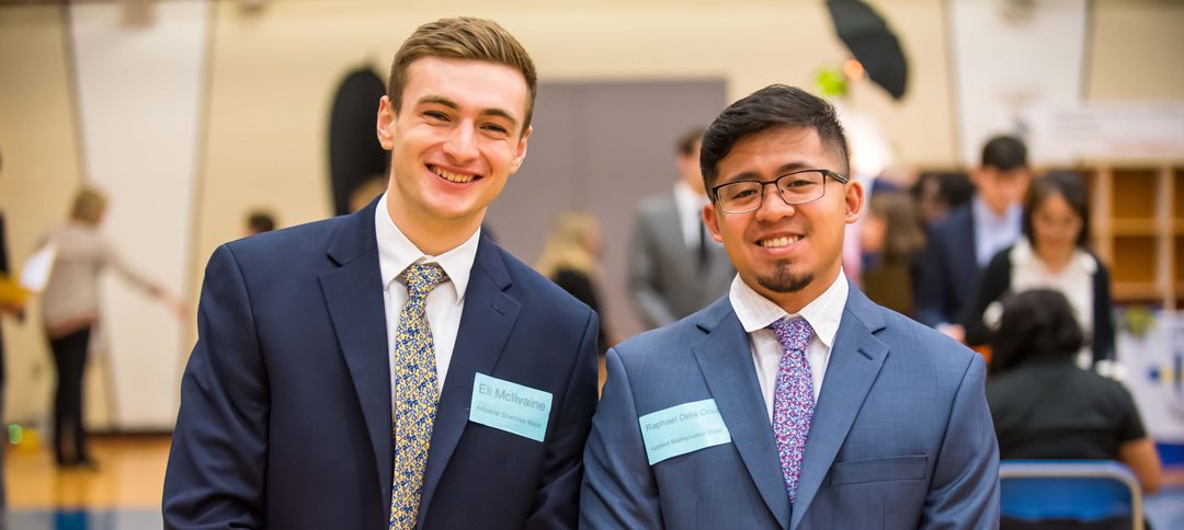Two male students in suit and tie smiling at the camera at a Career Fair event