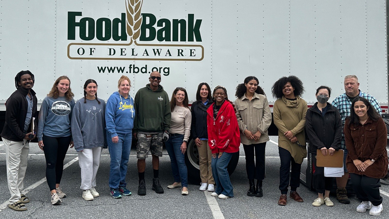 13 volunteers pose in front of a Food Bank of Delaware truck at a Mobile Food Pantry event