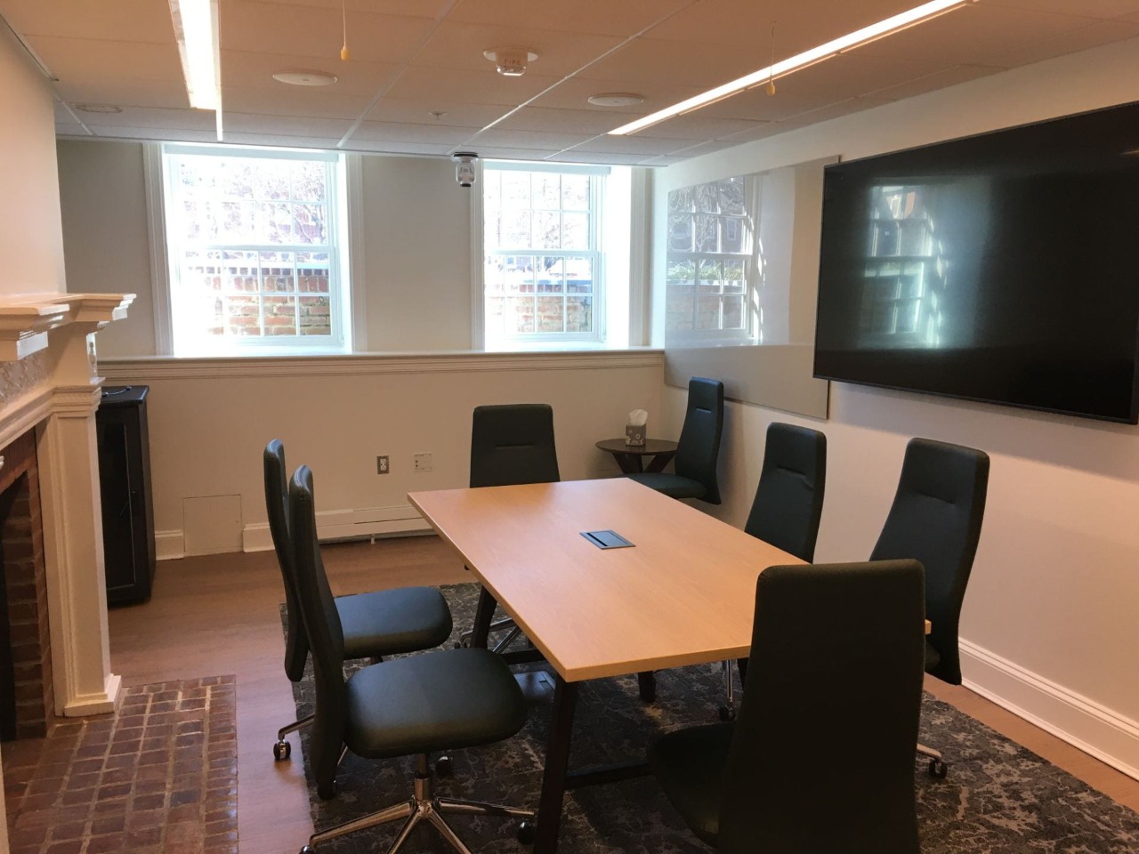 Small conference room with fireplace, rectangular table and high-backed chairs, large display monitor and glass writing board