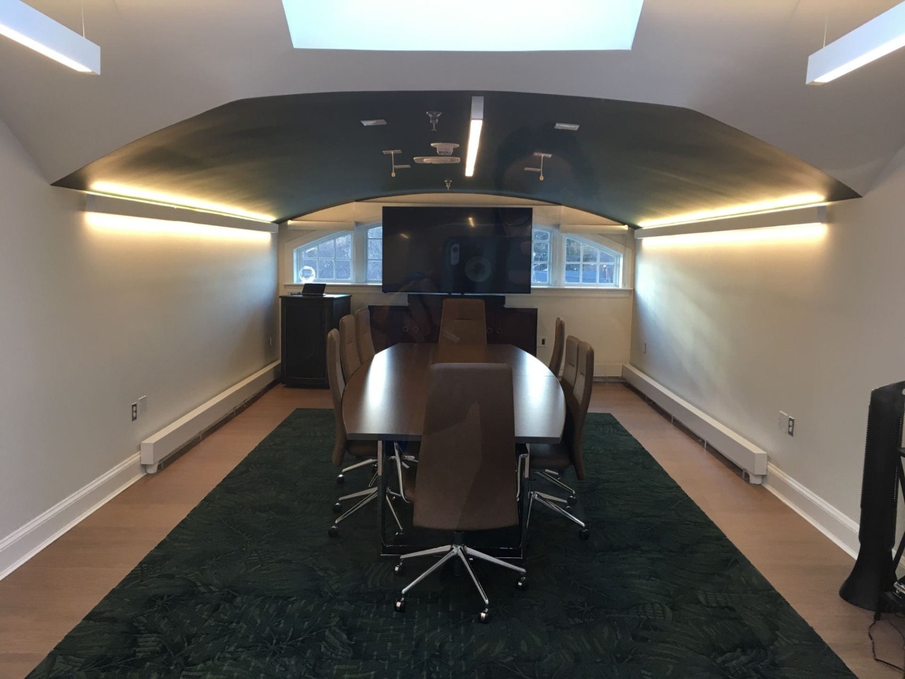Conference room with long table and eight chairs, with a digital display at the front
