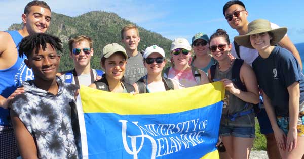 A group of Global Studies students abroad, holding a University of Delaware flag