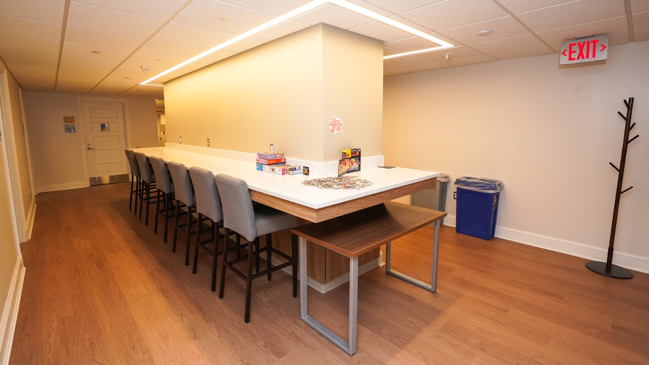a table in the middle of the room with chairs surrounding and boxed puzzles on the table.