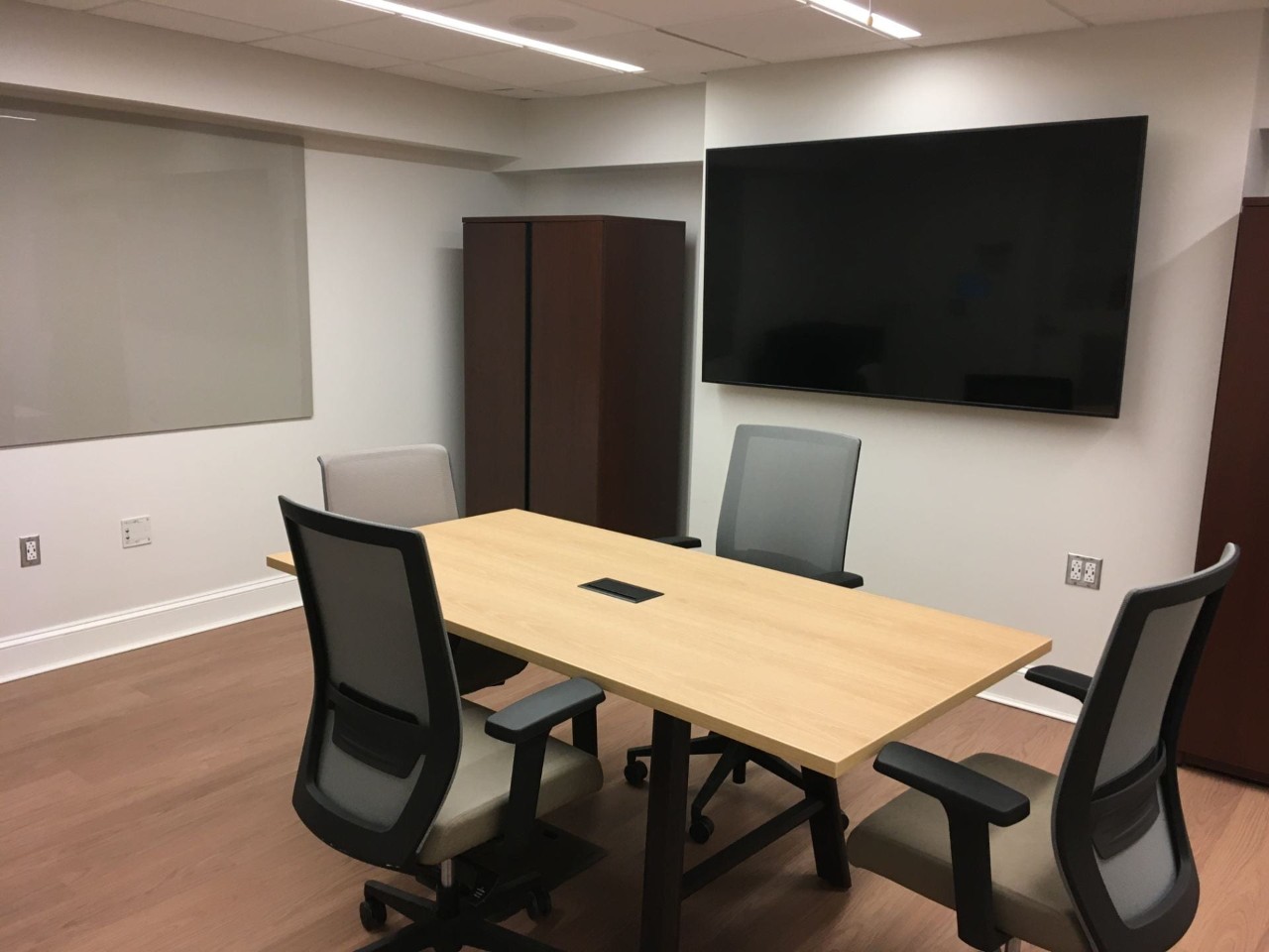 Small meeting room with four chairs around a table, large digital display and glass writing board