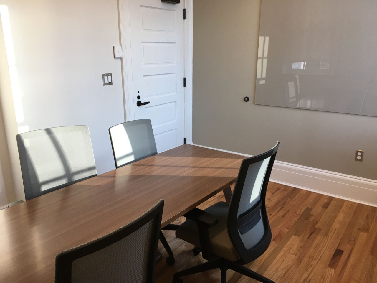 Small meeting room with rectangular table, chairs and glass writing board