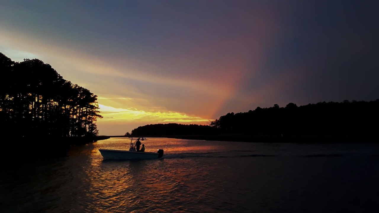 Photograph of two people on a boat, silhouetted in the sunset on a tranquil bay