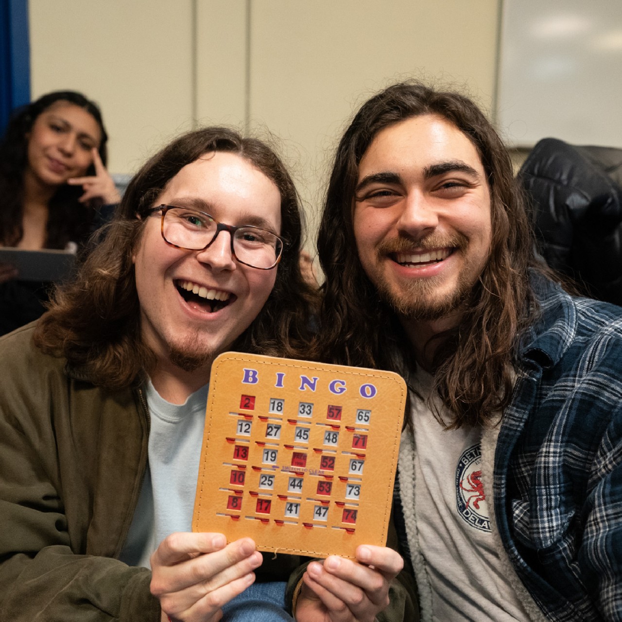 two students hold up a bingo card and smile