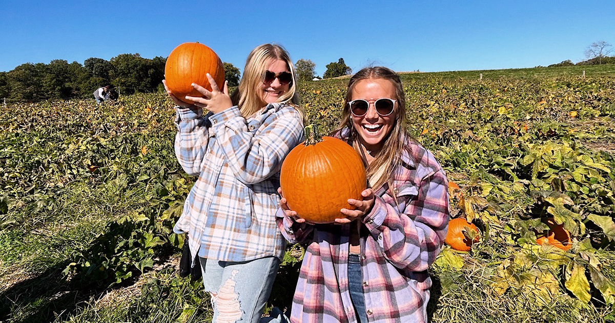 students in flannel shirts pose in a pumpkin patch holding pumpkins they've recently picked