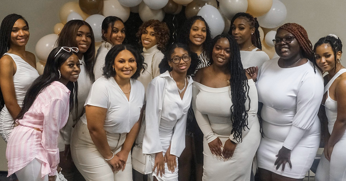Sisters on the Move members pose in white clothing in front of a balloon arch
