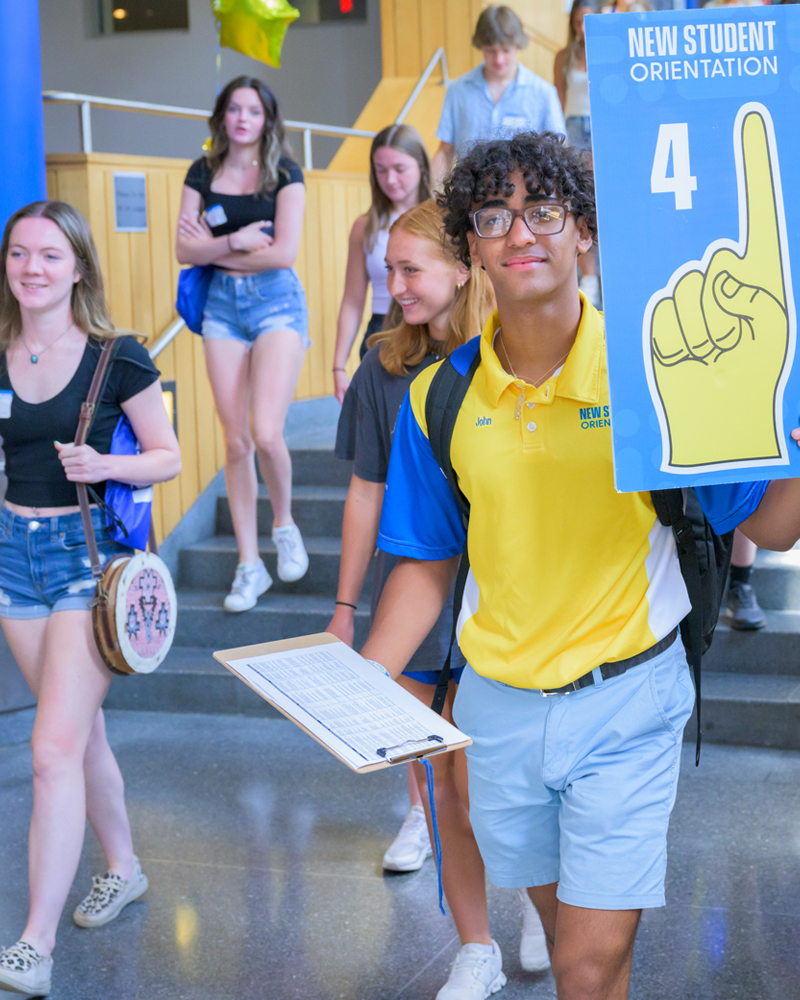 an Orientation Leader leads an NSO group through Trabant Student Center, holding a sign with a pointing finger and #4