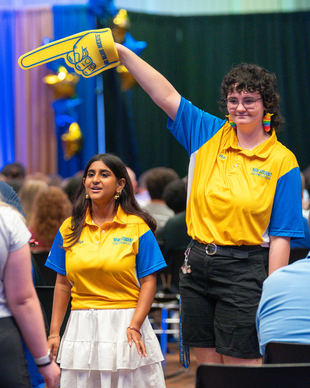 two Orientation Leaders show families to their seats, one wearing a giant foam finger.