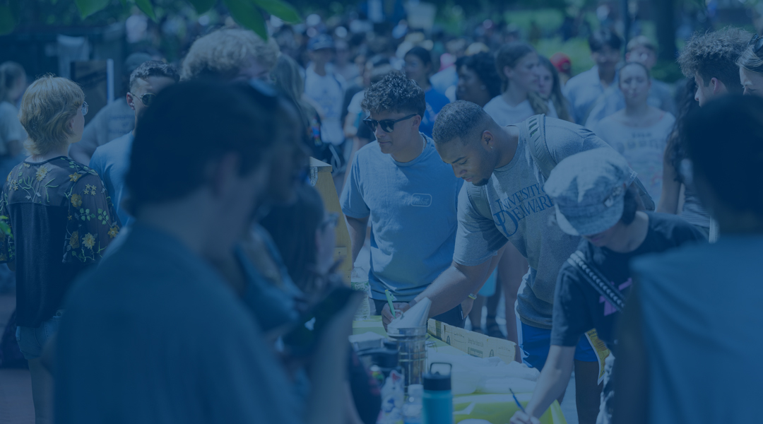 among a crowd, a student signs up for a club at UD's Involvement Fair