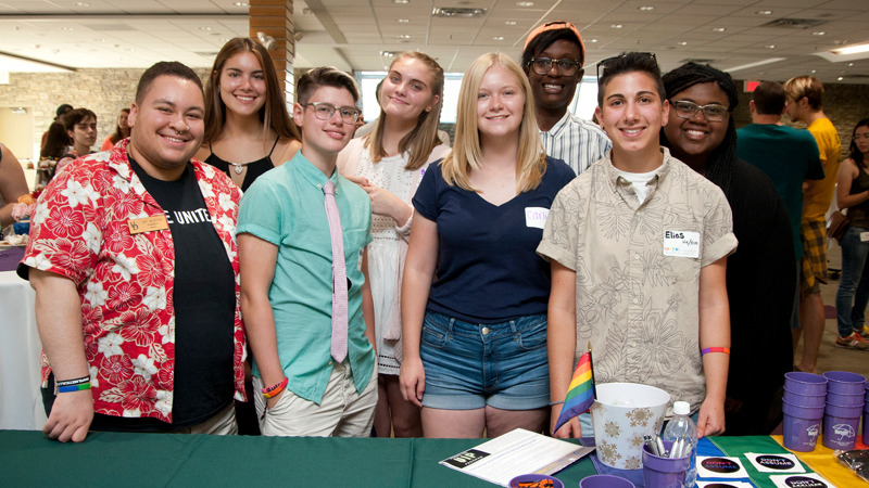 a group of students pose, sitting on outdoor furniture outside a UD residence hall.