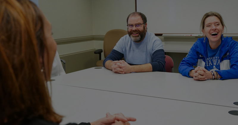 a smiling students sits at a table with smiling staff members of Community Standards & Conflict Resolution
