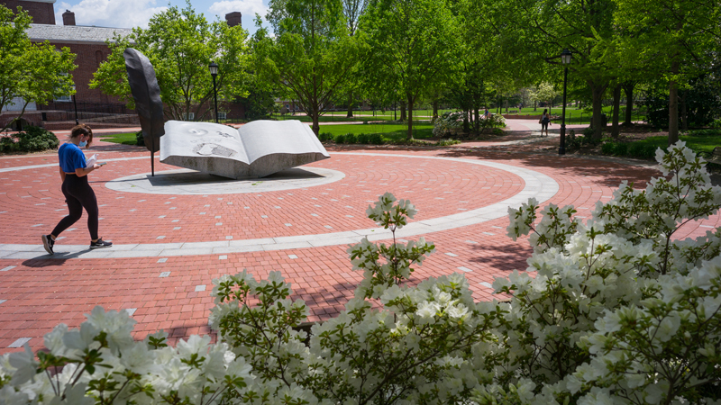 a student walks by the book statue in Mentors' Circle on a sunny day.