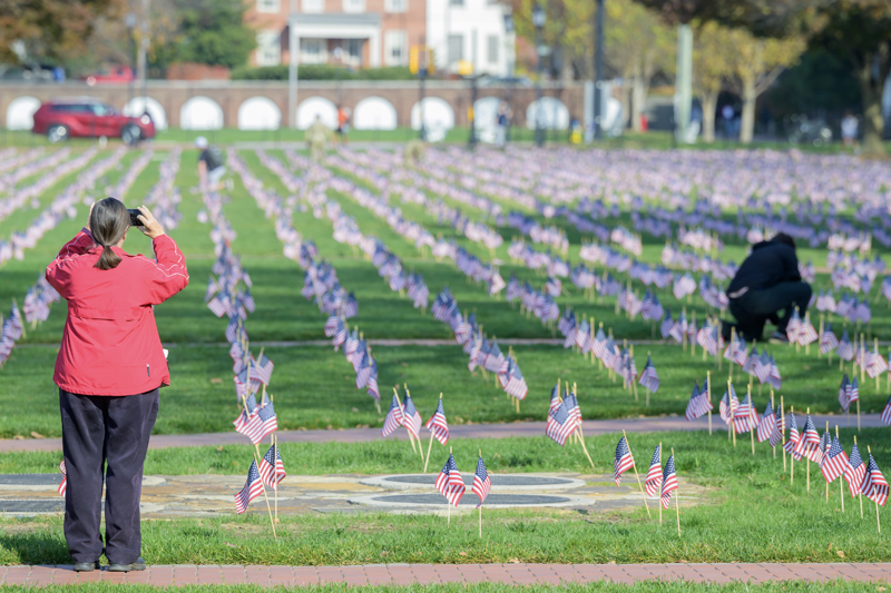 a person takes a picture of the grid of flags planted on the Green, while another person bends down to view a flag up close