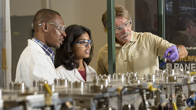 IEC-SunShot_Research-090616 Steve Hegedus, senior scientist in energy conversion, with students Ugochukwu Nsofor and Gowri Sriramagiri working on a project financed by the Department of Energy's (DOE) "SunShot Initiative." Overseen by the DOE's Solar Energy Technologies Office, SunShot funds cooperative projects which help to reduce the cost of solar power generation to a target of $0.06 per kilowatt-hour ($1 per watt) without additional incentives or subsidies. - (Evan Krape / University of Delaware)