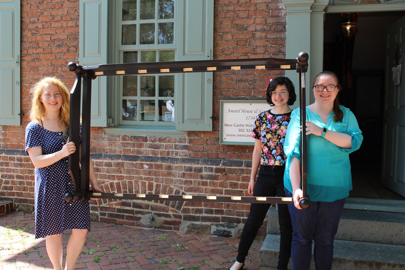 Students (from left) Savannah Kruguer, Amy Ciminnisi and Sara McNamara carry the replica trundle bed frame they created into the Amstel House in New Castle, where it will be displayed.