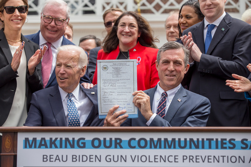 Delaware Gov. John Carney (right), with assistance from former Vice President Joe Biden, holds the legislation he signed on Monday putting into state law restrictions on gun access to people health professionals believe present a danger to themselves or others. 