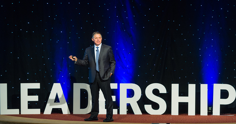 UD Alumnus Robert Siegfried stands on a stage, with the words leadership behind him, while speaking to the audience at the Fall 2018 Siegfried Youth Leadership Program