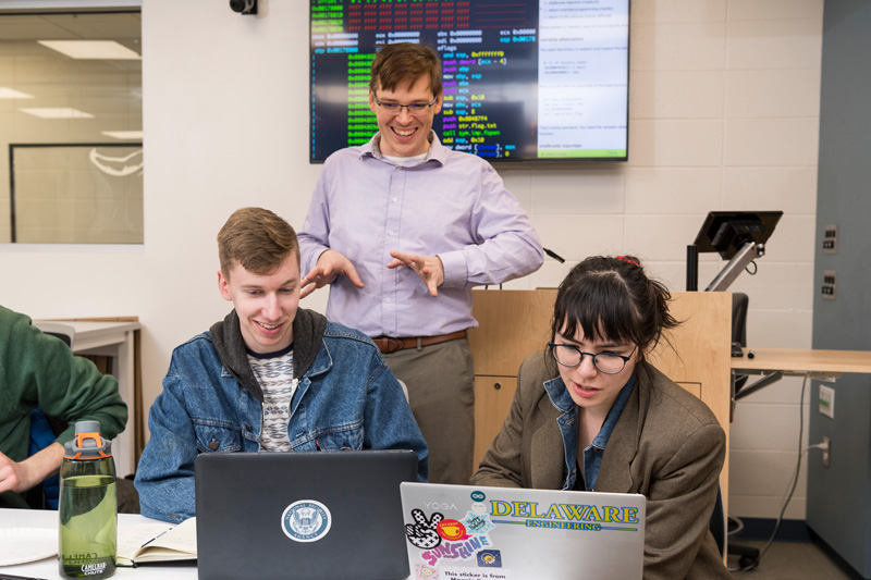 Dr. Andy Novocin teaches students developing and practicing cybersecurity skills to make them more “ethical” hackers in the world of cybersecurity in the iSuite at Evans Hall, Friday, March 22nd, 2019.  Students are: Dan Goodman (gray long sleeve), Vineeth Gutta (black shirt, khakis), Landon JOnes (black jacket), Ryan Geary (green crewneck), Thomas Pisklak (striped t-shirt), Isabel Navarro (red pants, brown blazer), Collin Clark (jean jacket, nose piercing), And Alena Gusakov (red shirt, jeans)  (PHOTO RELEASES WERE OBTAINED ON ALL PICTURED.)