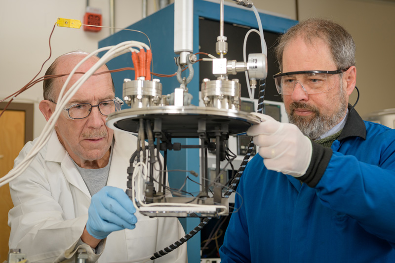 Brian McCandless (blue lab coat) is an associate scientist with the Institute of Energy Conversion (IEC) who's work focuses on "deposition and analysis of compound semiconductor thin films and devices photovoltaics" [IEC website]. In collaboration with Wayne A. Buchanan, research associate II at the IEC (white lab coat), he's been working on developing an improved vapor transport reactor deposition head design to allow for large-scale production of thin film photovoltaics. - (Evan Krape / University of Delaware)