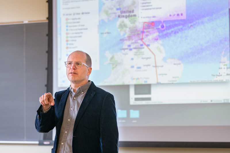 Assistant Professor Paul Jackson teaching a section of his GEOG 345: "Cultural Geography" class in which students were broken into two groups to play a "care or kill" turn-based role-playing game. The students in the class were divided into two groups - a "kill" group which tried to theoretically "kill" a fictionalized version of Prof. Jackson by changing his geographic location or demographic identify (age, nationality, gender, etc.) and a "care" group which would attempt to save him by modifying the same characteristics. The teams would role dice to determine the degree to which each would be permitted to change variables in the game. - (Evan Krape / University of Delaware)