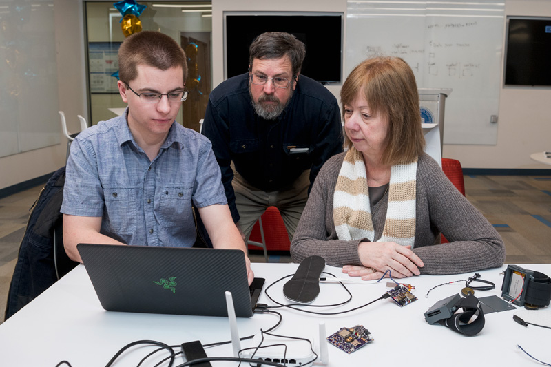 Resonate Forward, a startup that grew out of former UD faculty member Ingrid Pretzer-Aboff’s work on a Parkinson’s Disease (PD) shoe, is being awarded a $440k grant from the Michael J. Fox Foundation [embargoed news] to develop a vibratory device for people with PD who experience a freezing of gait, a phenomenon where the patient gets “stuck” and cannot move their feet.  The grant is part of a new funding initiative by MJF Foundation to test non-pharmacological interventions for the treatment of gait and balance disturbances in people with PD.  Ingrid Petzer-Aboff (only female, tan sweater/scarf) started the project at UD and is now at Virginia Commonwealth but still working closely with Theo Fleck, (grayish blue shirt) a UD junior computer engineering major who is working on the device components and integrated software, Rick Martin, associate professor, electrical and computer engineering and mentor to Fleck, and Scott Jones, professor of accounting in the Department of Accounting & Management Information Systems in Lerner (black shirt). (Releases were obtained on anyone pictured.)