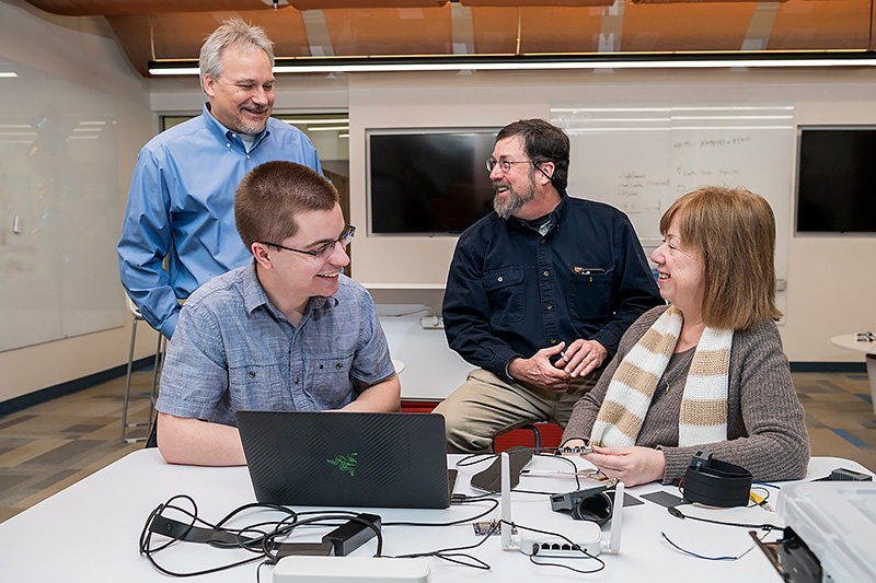 Resonate Forward, a startup that grew out of former UD faculty member Ingrid Pretzer-Aboff’s work on a Parkinson’s Disease (PD) shoe, is being awarded a $440k grant from the Michael J. Fox Foundation [embargoed news] to develop a vibratory device for people with PD who experience a freezing of gait, a phenomenon where the patient gets “stuck” and cannot move their feet.  The grant is part of a new funding initiative by MJF Foundation to test non-pharmacological interventions for the treatment of gait and balance disturbances in people with PD.  Ingrid Petzer-Aboff (only female, tan sweater/scarf) started the project at UD and is now at Virginia Commonwealth but still working closely with Theo Fleck, (grayish blue shirt) a UD junior computer engineering major who is working on the device components and integrated software, Rick Martin, associate professor, electrical and computer engineering and mentor to Fleck, and Scott Jones, professor of accounting in the Department of Accounting & Management Information Systems in Lerner (black shirt). (Releases were obtained on anyone pictured.)