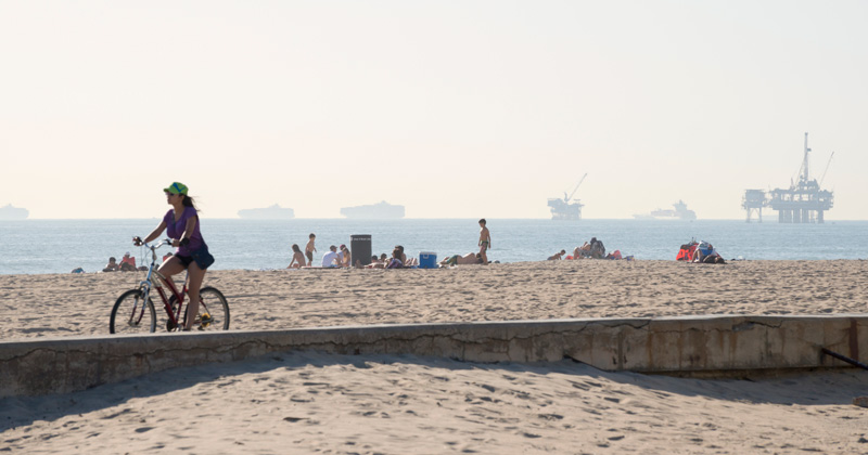 468474116 Beyond the bikeway and beach at Huntington Beach in Orange County, California, oil rigs rise from the ocean and container ships wait to enter the nearby port of Long Beach