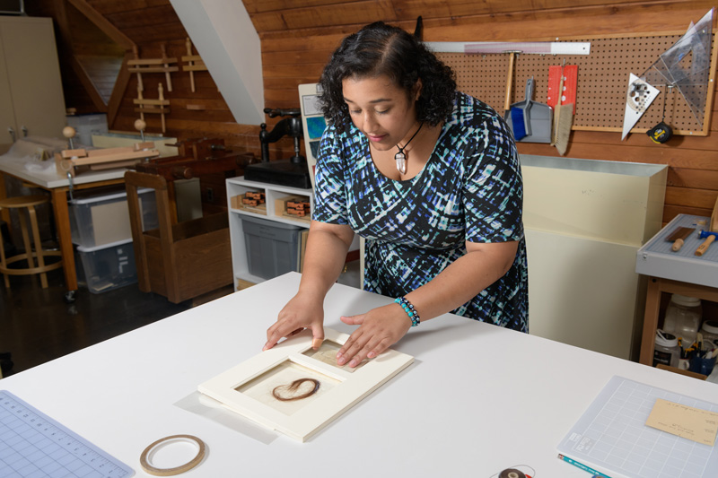 Layla Huff (blue, white, black patterned dress) is an undergraduate student at Morgan State University who has been studying art conservation at Winterthur for an internship in the summer of 2019. Working with mentor Melissa Tedone, Huff has been preparing a lock of hair for exhibition in England. The hair comes from Elizabeth “Lizzie” Siddall, an English artist, poet, and artists' model. Until her husband, painter Dante Gabriel Rossetti, made her his exclusive model, Lizzie frequently modeled for drawing and paintings by the Pre-Raphaelite Brotherhood. The lock of hair comes from the Mark Samuels Lasner Collection (MSL Coll 6690) and was a "surprise" found among a collection of items purchased for the collection.