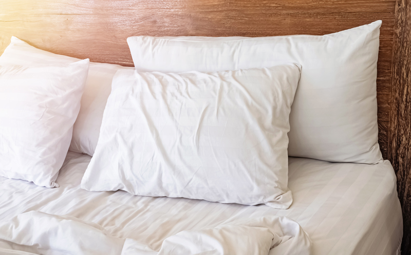 1138434690 Pillows on the bed with white bedlinen and wooden bedhead onthe sunny morning