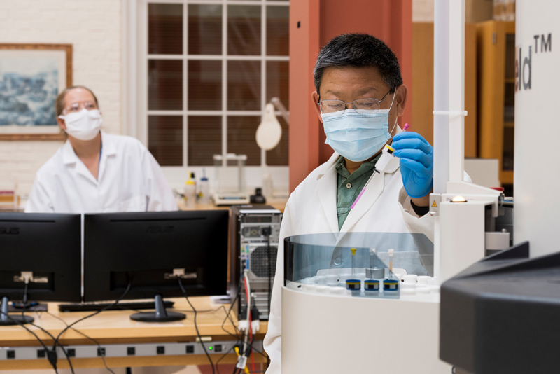 Dr. Steve Bai works in the NMR Lab with colleagues Martin Maxwell (blue labcoat) and Caitlin Quinn (white labcoat, ponytail) who have been working all through the COVID pandemic to make sure research samples and work still get processed and resulted. 
