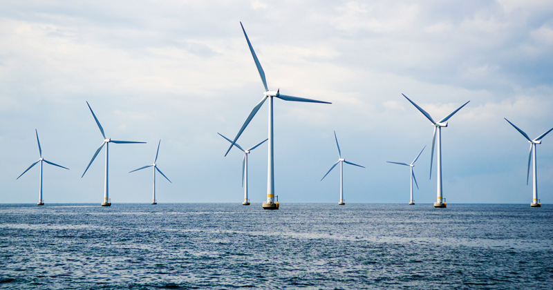 Nine wind turbines at sea. Windmills in blue ocean with a clouded blue sky.