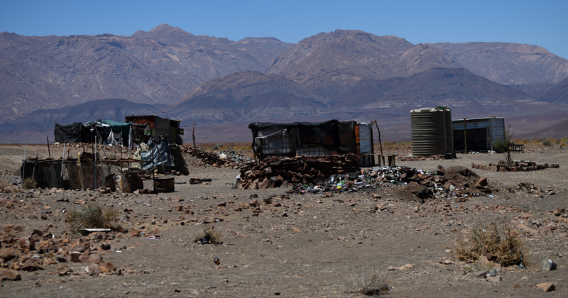 The mine is worked by just a few miners, who dig by hand. The shacks are shown in the centre of the photo, and reveal the extreme poverty and isolation that the miners live in. Mountains are shown in the distance. 

Gobogobos is an area west of Brandberg Mountain in the Erongo region of Namibia. The area is famous for its crystals. The photo was taken in February 2018.