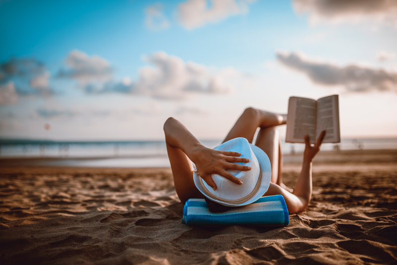933846814 Female Reading and Enjoying Sunset on Beach by the Ocean