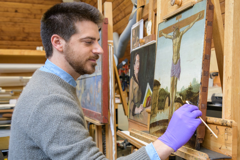 Class of 2021 Winterthur / University of Delaware Program in Art Conservation (WUDPAC) students working on conservation and preservation projects at the Winterthur Museum and Gardens Library.Pictured: Isaac Messina (second-year WUDPAC graduate fellow and painting major, Class of 2021): Surface cleaning a fifteenth-century Italian panel painting