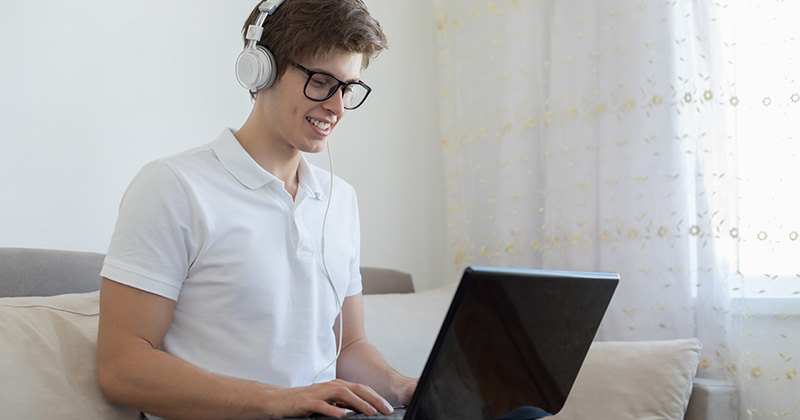 Male student sitting on couch working on laptop