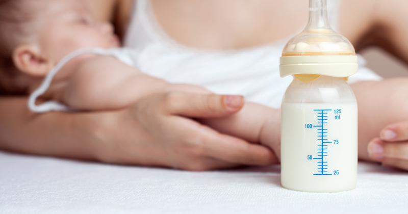 Mother holding a baby and bottle with breast milk for breastfeeding at foreground, mothers breast milk is the most healthy food for newborn baby