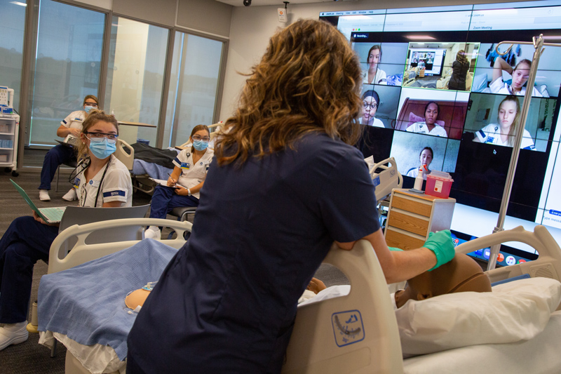 CHS-Nursing_Sim_Zoom-090920 April Prior, simulation lab instructor, teaches half her nursing undergrad class live in the 4th floor sim lab in the Tower at STAR while the other half of her students watch live and participate over Zoom.