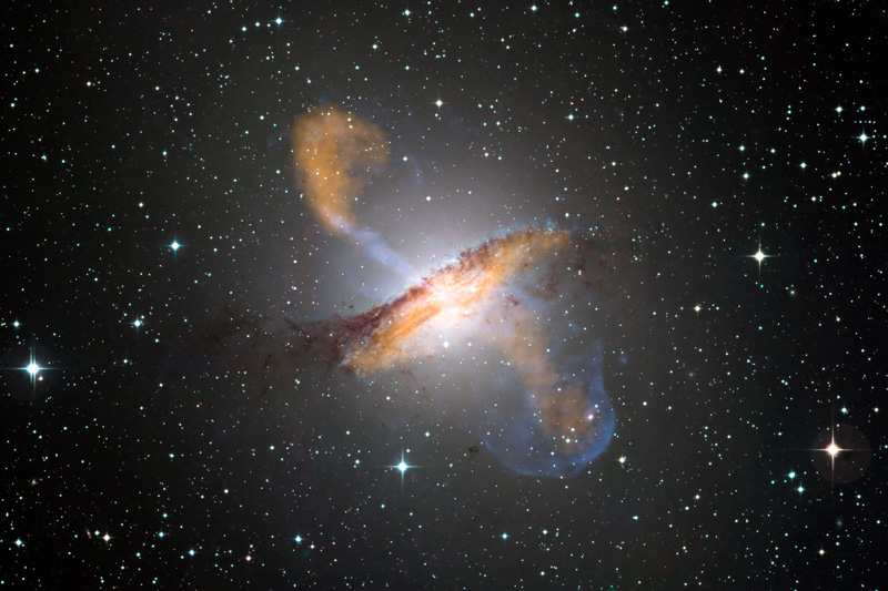 Colour composite image of Centaurus A, revealing the lobes and jets emanating from the active galaxy’s central black hole. This is a composite of images obtained with three instruments, operating at very different wavelengths. The 870-micron submillimetre data, from LABOCA on APEX, are shown in orange. X-ray data from the Chandra X-ray Observatory are shown in blue. Visible light data from the Wide Field Imager (WFI) on the MPG/ESO 2.2 m telescope located at La Silla, Chile, show the stars and the galaxy’s characteristic dust lane in close to "true colour". #L