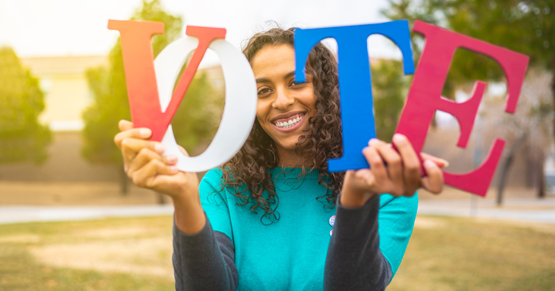 Holding VOTE letters colored in Red, White and Blue.