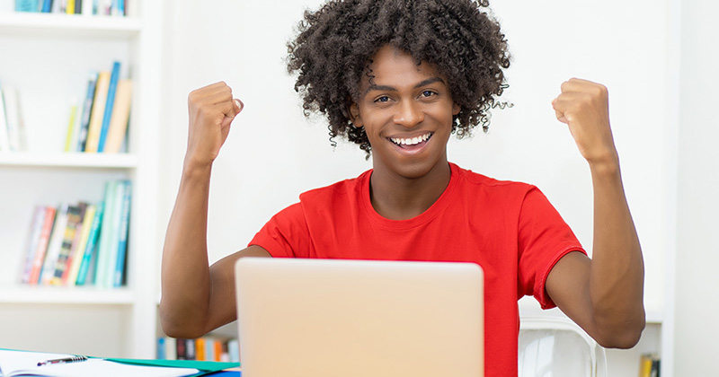 Happy male high school student on laptop with arms raised