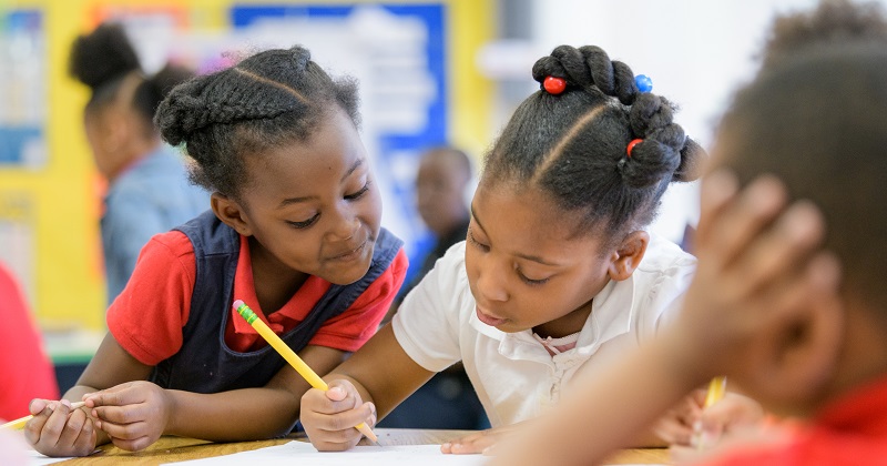 Three students from a racially underrepresented background work together on a written assignment in an elementary school classroom. 