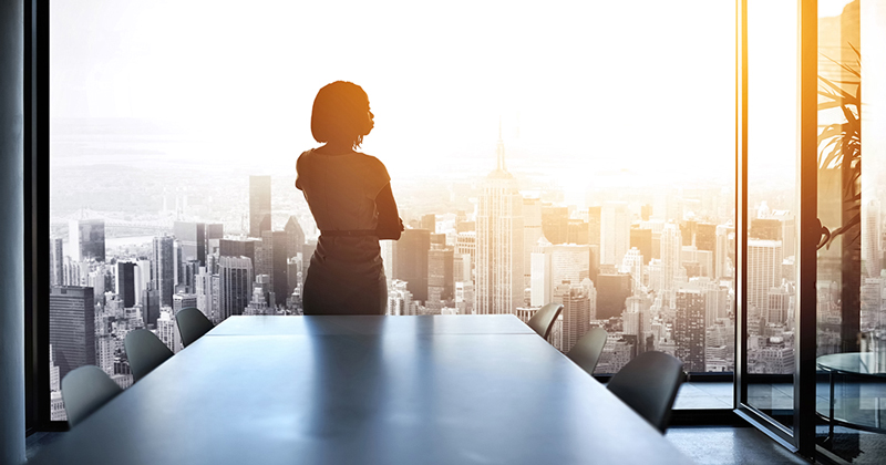 640189368 Rearview shot of a young businesswoman looking out from a large window in the office