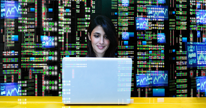 Woman on laptop with wall of data behind her