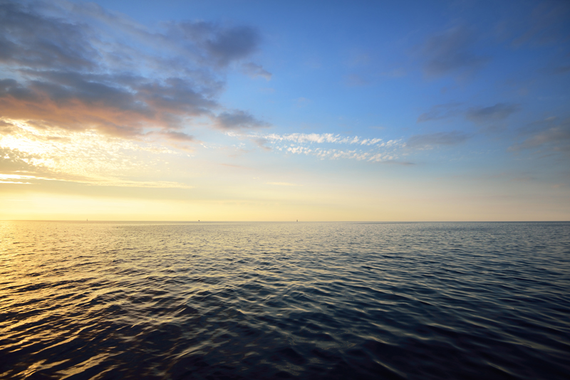 Sunset in a cloudy sky over open Baltic sea with veri distant ship silhouettes.