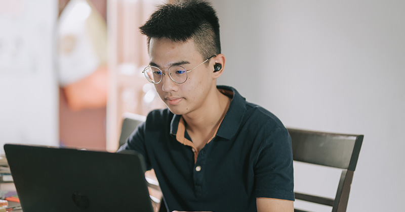 Male teenager sitting at table working on laptop