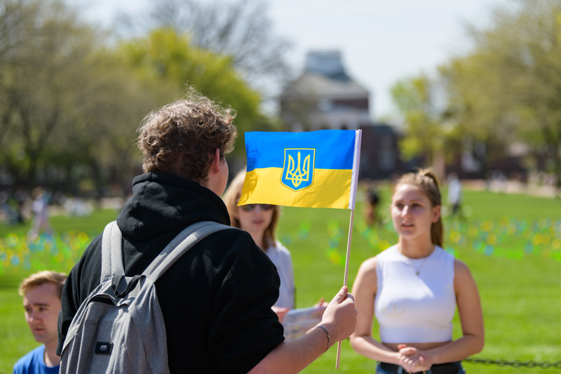 Brendan Czuczuk, a sophomore political science major whose family comes from Ukraine, waves the Ukrainian flag at the Stand with Ukraine fundraiser held on Friday, April 22. The event was organized by members of the Russian club, including president Lily Markow, right, a senior Russian studies and criminal justice double major.